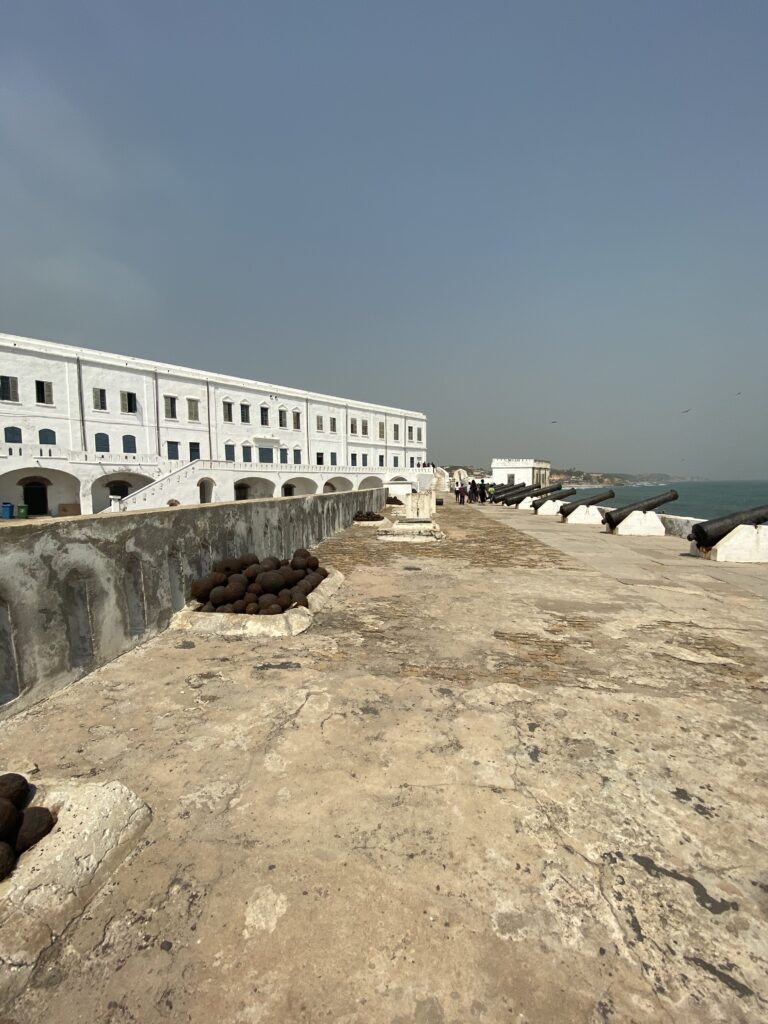 The rampart of Elmina Castle in the Gold Coast in Ghana. In view are the white walls of the castle, cannon balls and cannons facing the Atlantic Ocean