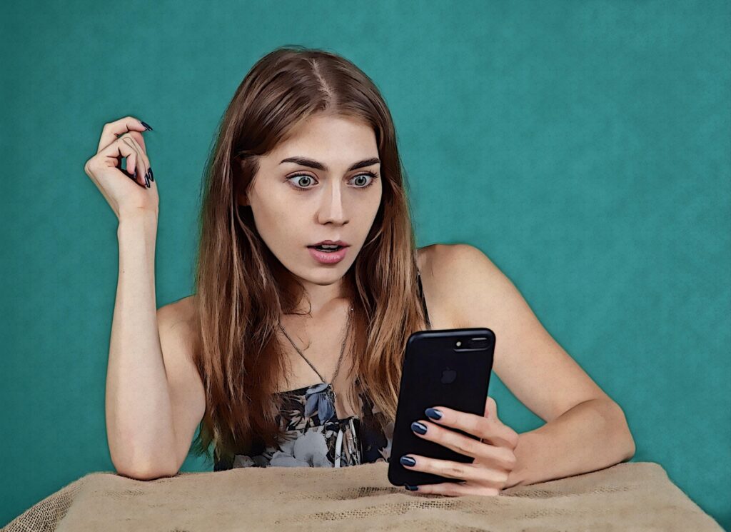 Viral art moments since 2020 have had art collectors' tongues wagging. In this image is a young woman who is sitting at a table and looking at her mobile phone with a surprised facial expression.