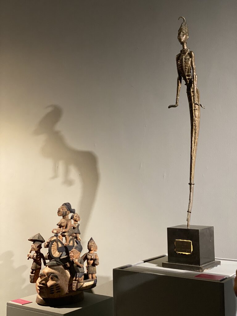 This image shows one of Ben Enwonwu's famous bronze sculptures. It is featured next to a traditional masquarade headdress. Ben Enwonwu is a Nigerian modernist. 