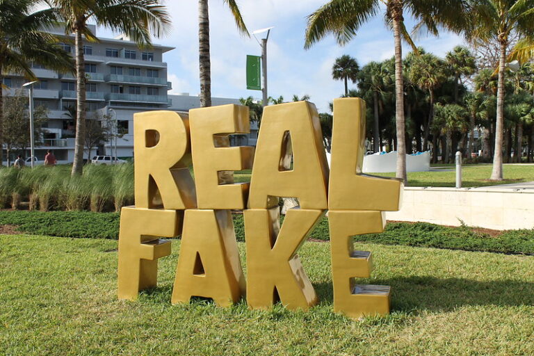 A sculpture of gold text with the words REAL FAKE stacked on top of one another, set on grass at Art Basel Miami